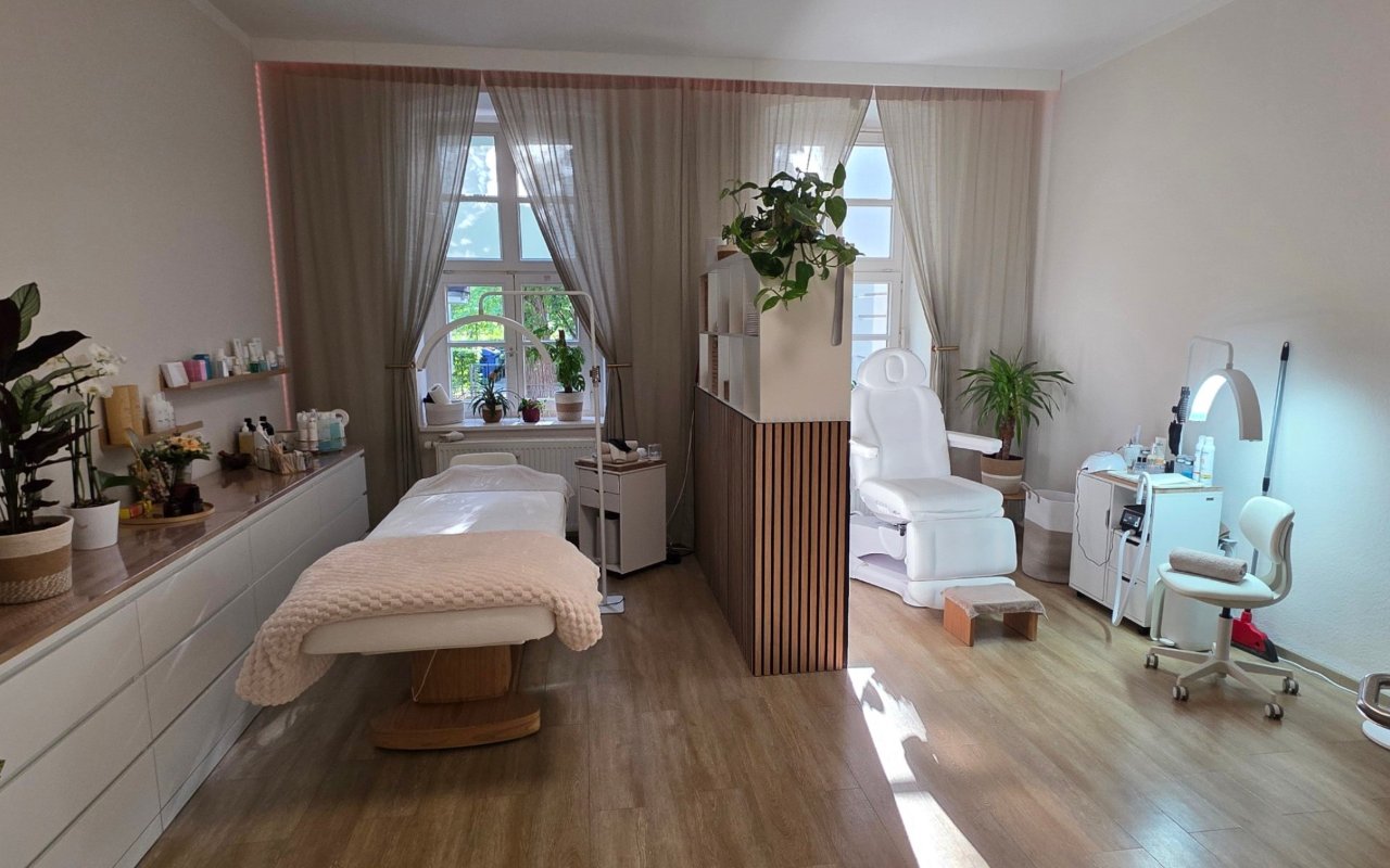 Heller Behandlungsraum mit Kosmetikliege, Fußpflegestuhl und Pflanzen